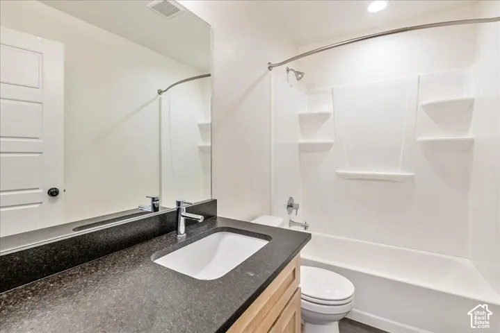 Bathroom featuring a full-width vanity mirror, dark countertop with an integrated sink, chrome faucet, wood-finish vanity cabinetry, and a white tub/shower combination with built-in shelving