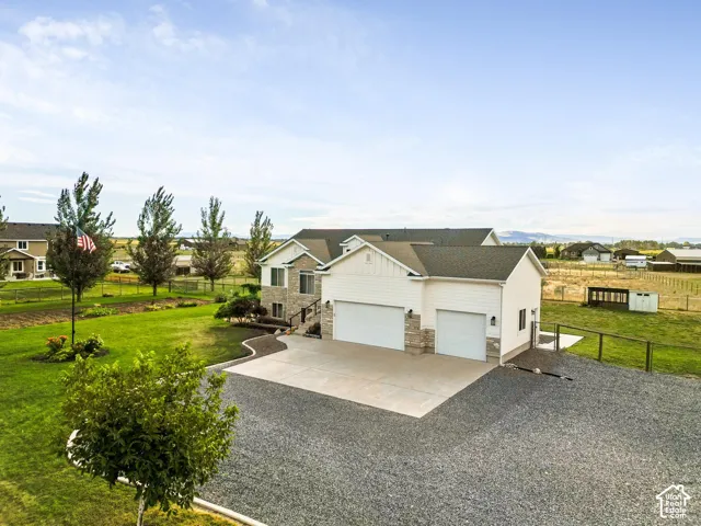 Two-story residence featuring white siding and stone accents, a two-car garage, and an expansive gravel driveway