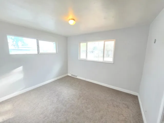 Neutral-toned wall paint, two large windows, one smaller window, overhead lighting fixture, and neutral carpet