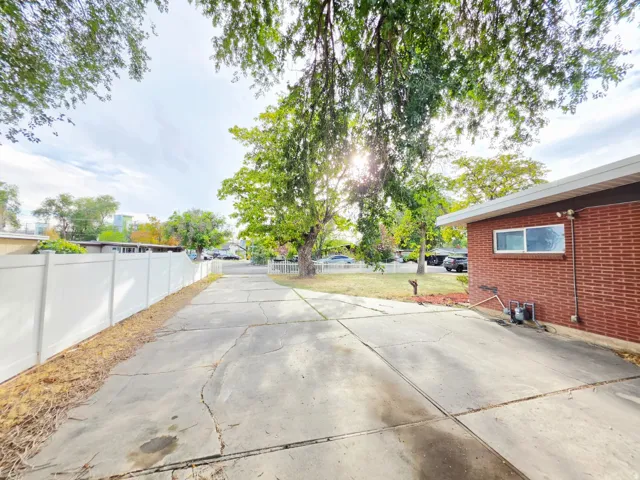 Brick exterior with white trim, concrete driveway, white privacy fencing, and mature trees