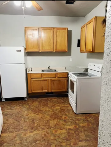 Kitchen featuring wood cabinetry, a stainless steel sink, white appliances, and a ceiling fan