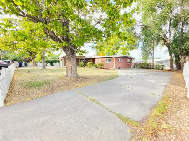 Brick exterior residence with a concrete driveway, a white picket fence, and mature trees