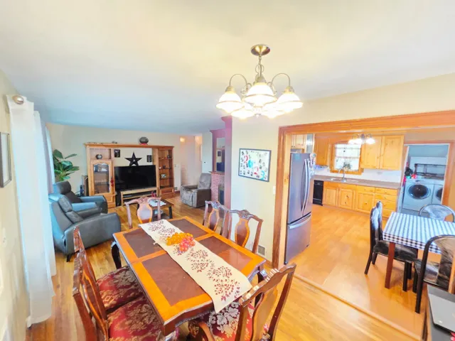 Hardwood-style flooring throughout, a dining area with a multi-bulb chandelier, and a kitchen featuring stainless steel appliances and wood cabinetry