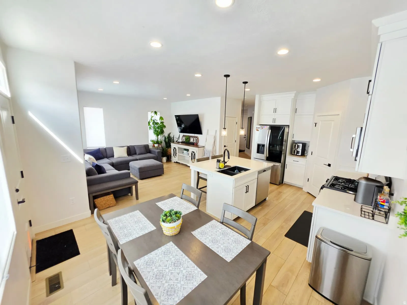 Open-concept living area with light wood-finish flooring, recessed lighting, and white walls