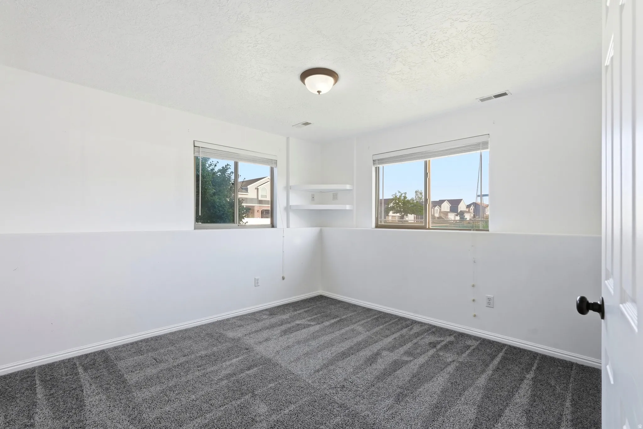 Recessed windows, wall-mounted shelving, overhead flush-mount lighting, and gray patterned carpeting