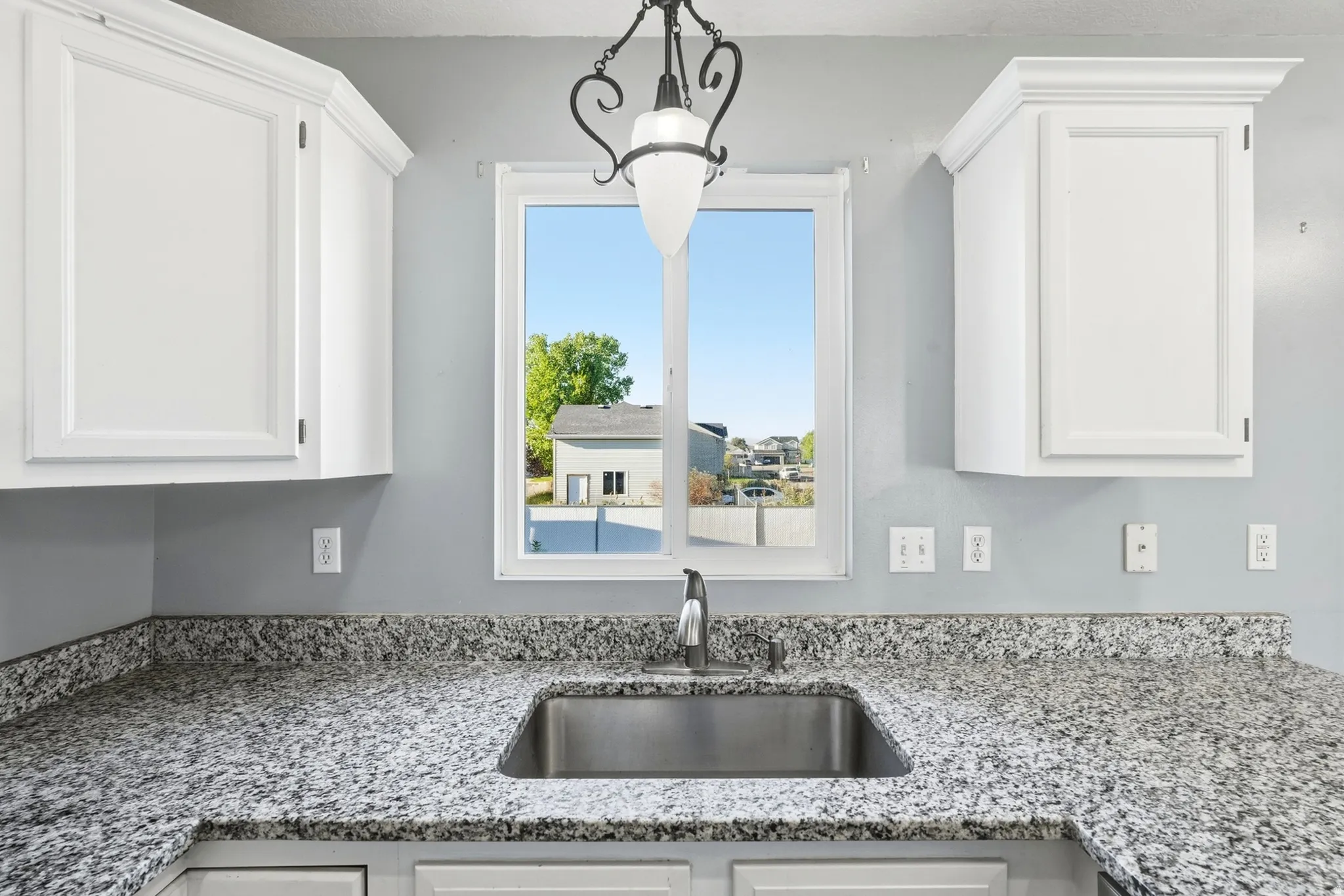 White shaker-style cabinetry, a stainless steel undermount sink, a chrome faucet, and speckled countertops