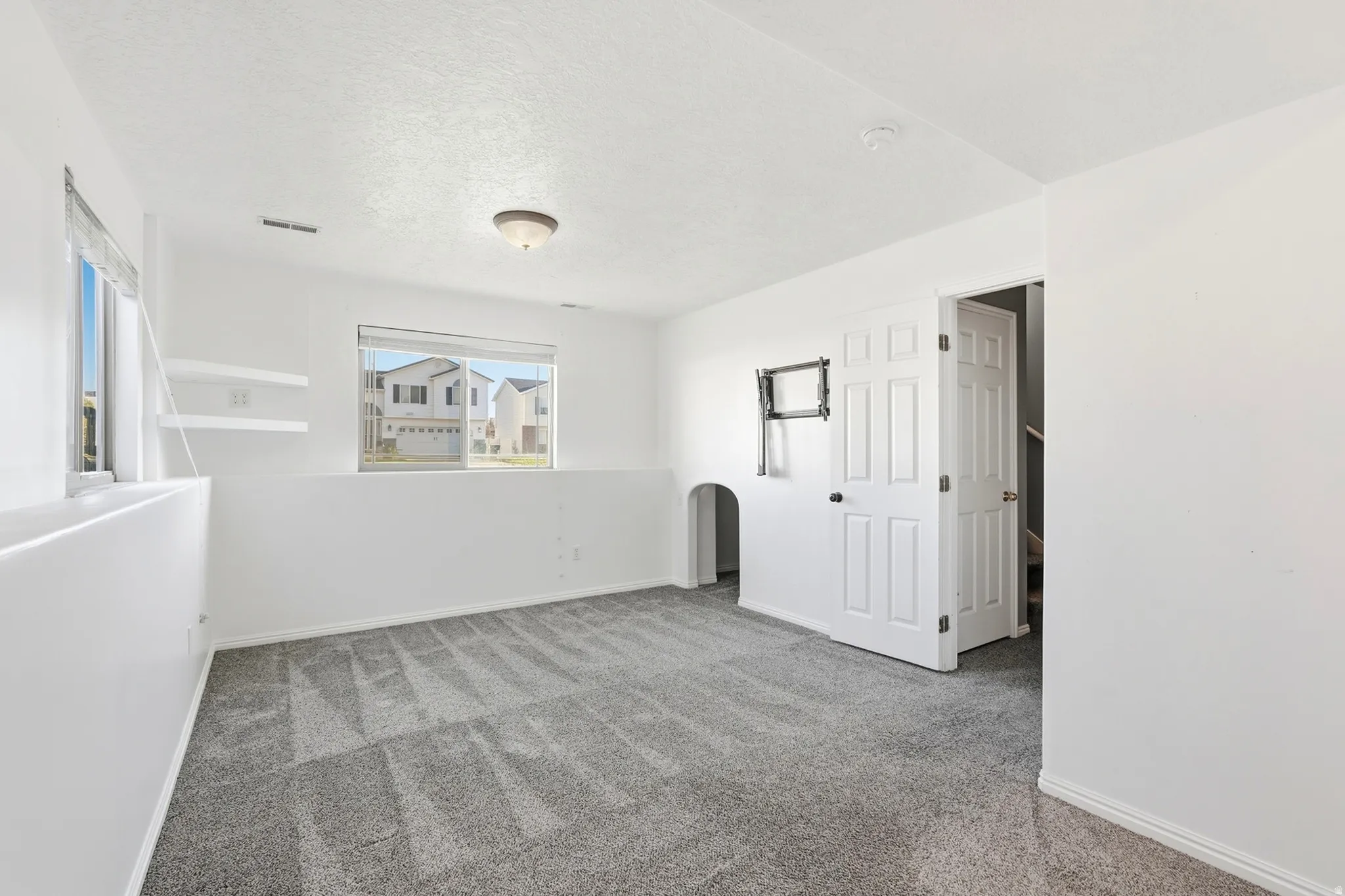 Carpeted room with white walls, two windows, two built-in floating shelves, and a paneled door