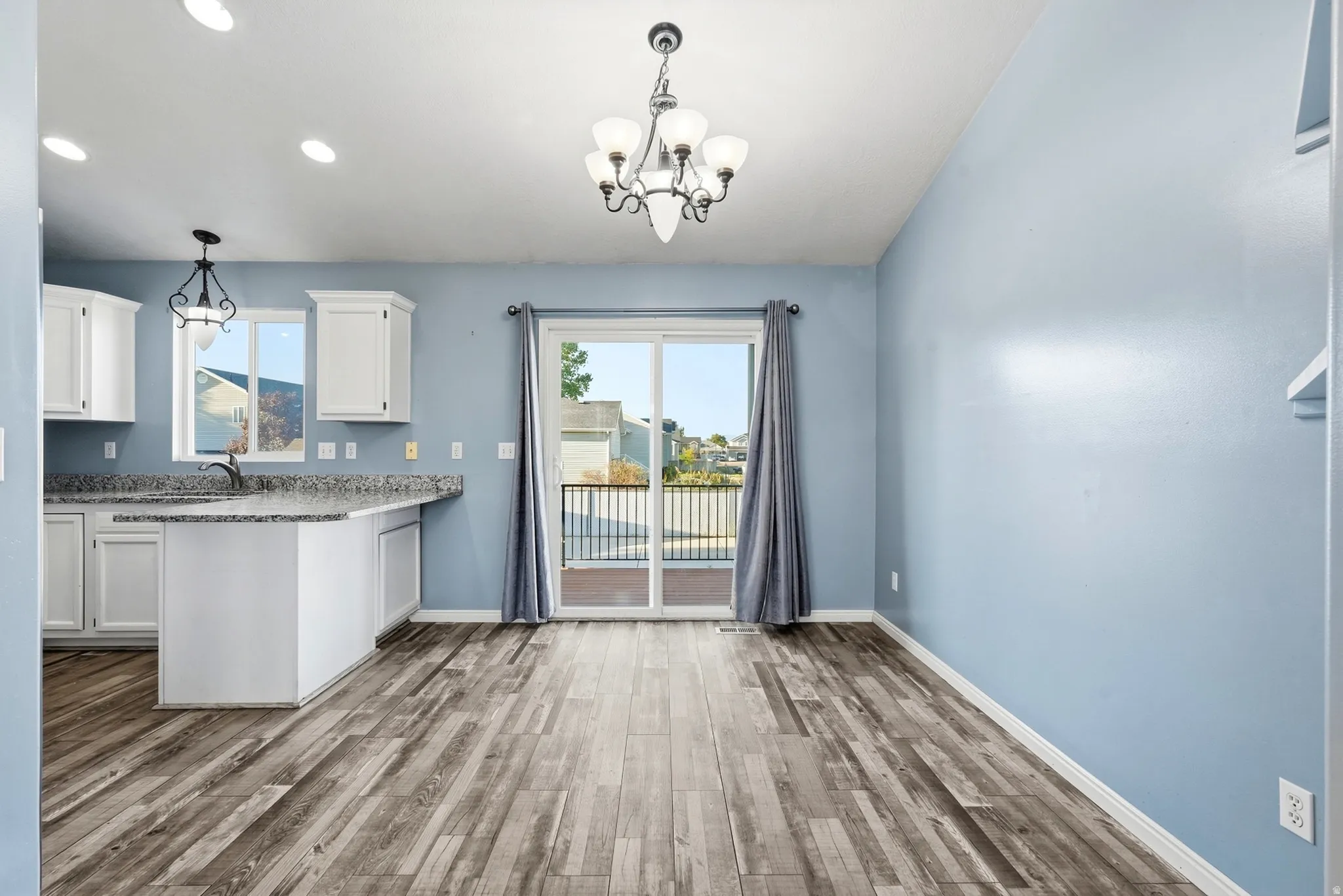 Spacious interior featuring wood-finish flooring, a kitchen with white cabinetry and a breakfast bar, and a sliding glass door opening to a deck
