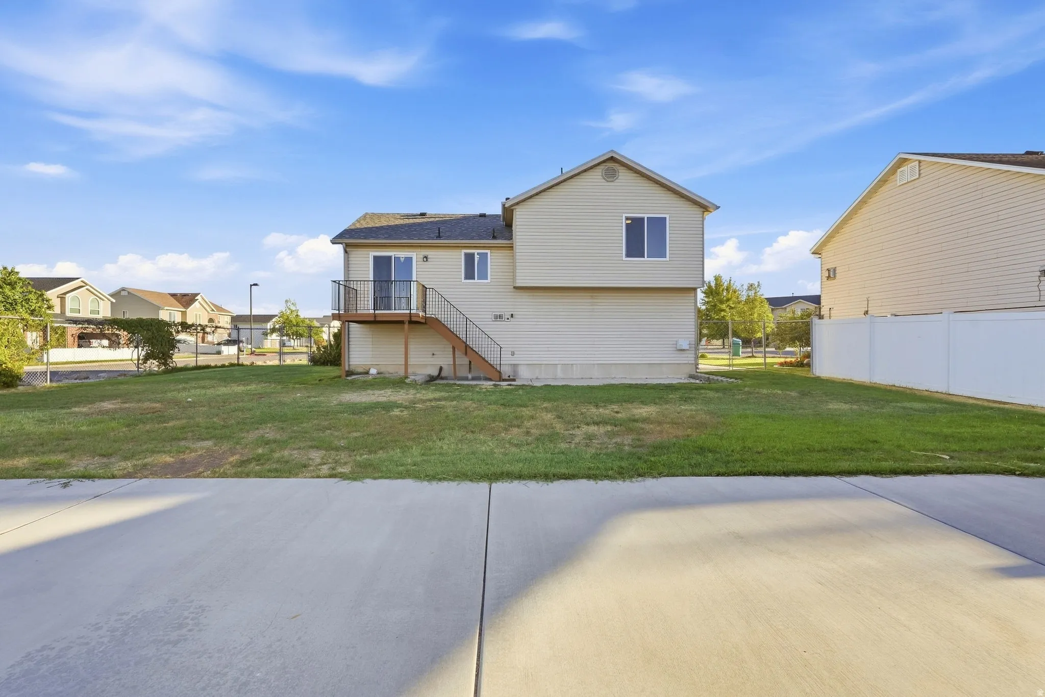 Two-story exterior with siding, featuring a second-story deck with metal railing and stairs, and a concrete patio