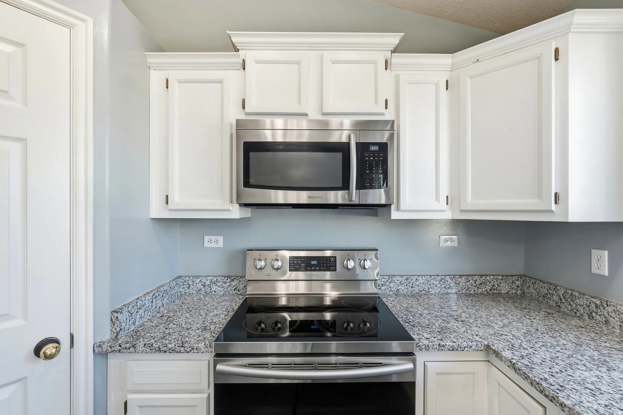 White upper cabinetry with crown molding, stainless steel microwave, stainless steel range with cooktop, and speckled countertops