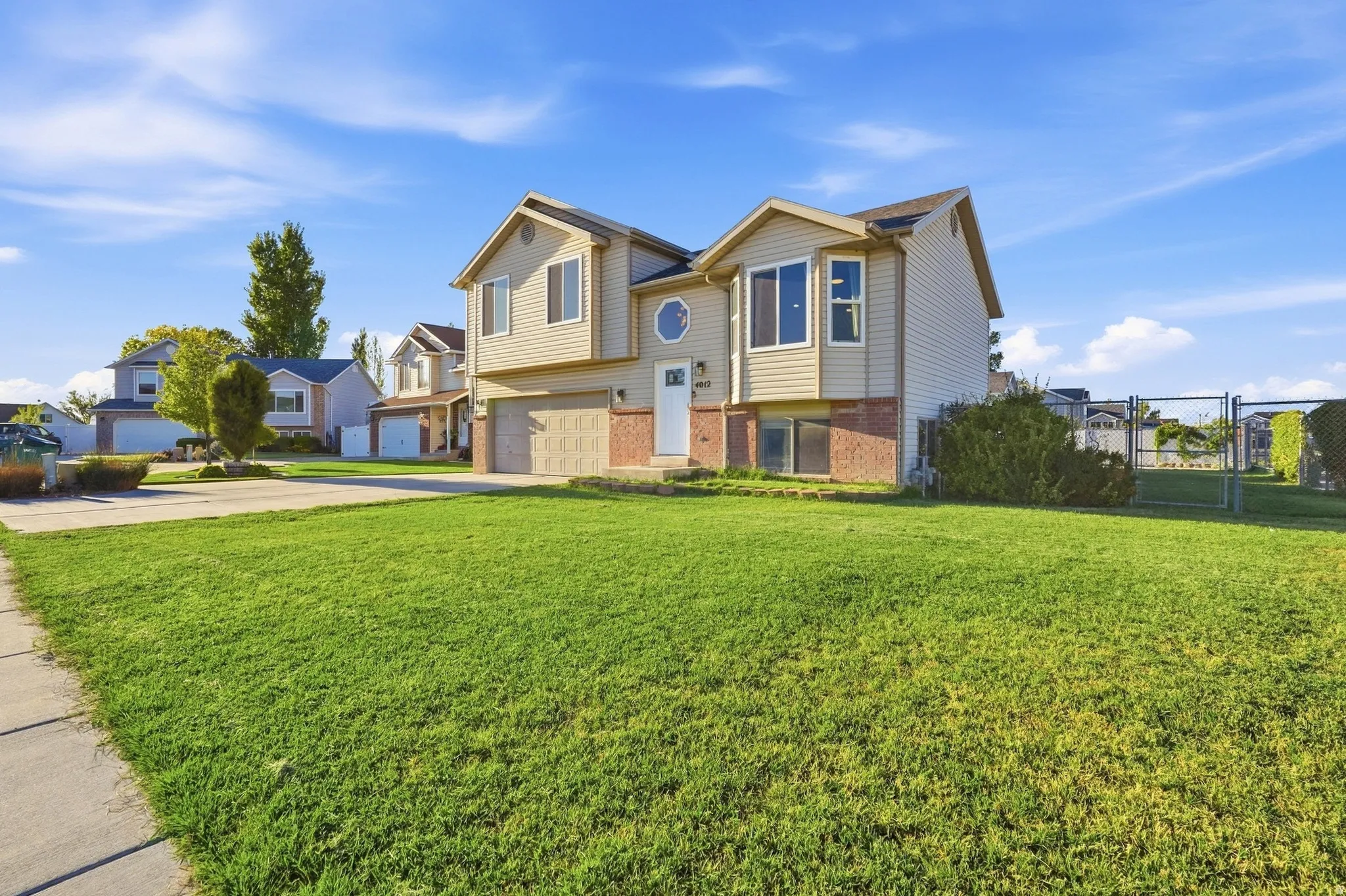 Two-story residence featuring light-toned siding, a brick foundation accent, an attached garage, a front-facing bay window, and an expansive front lawn