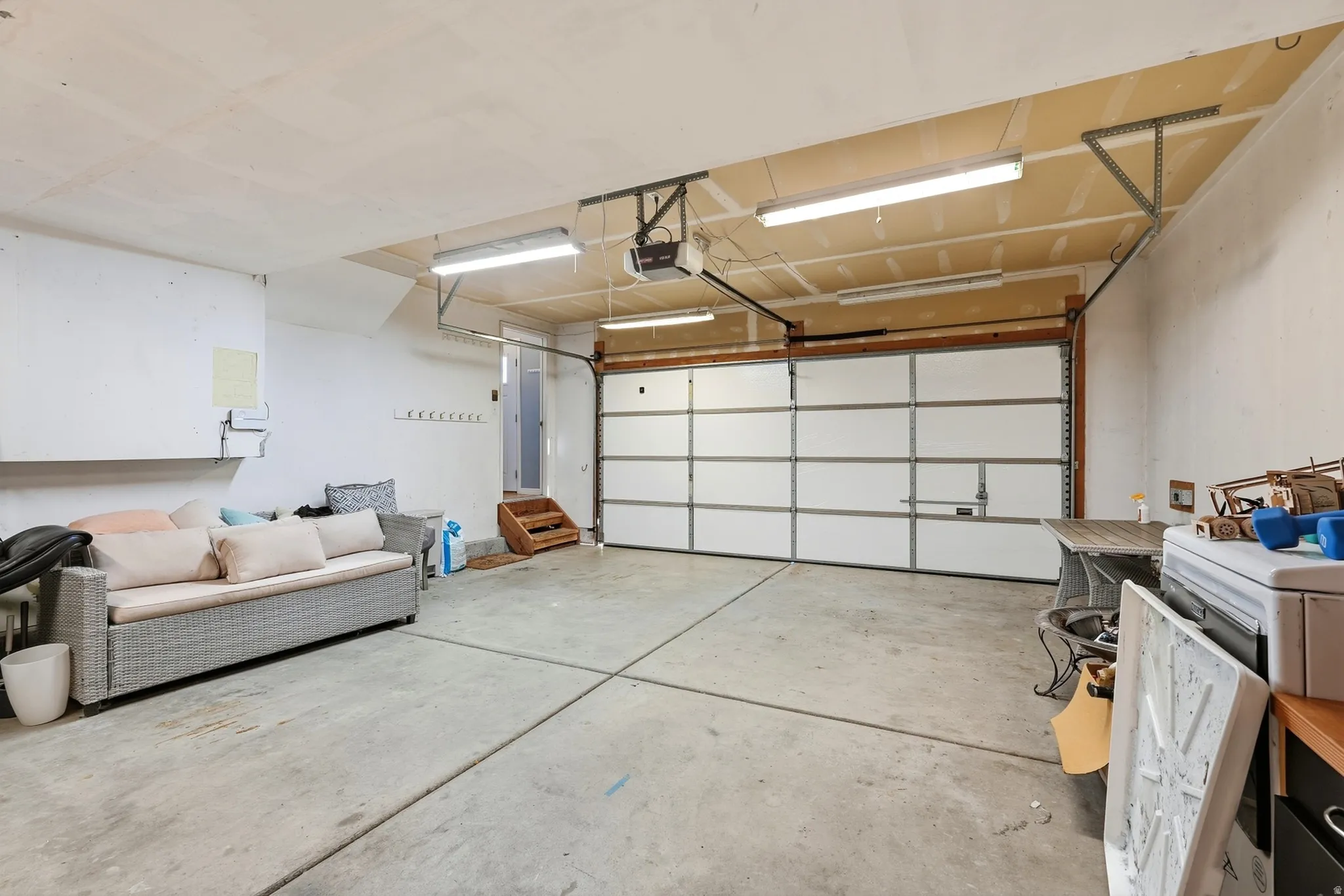 Spacious garage with a sectional garage door, concrete flooring, overhead fluorescent lighting, and visible ceiling joists