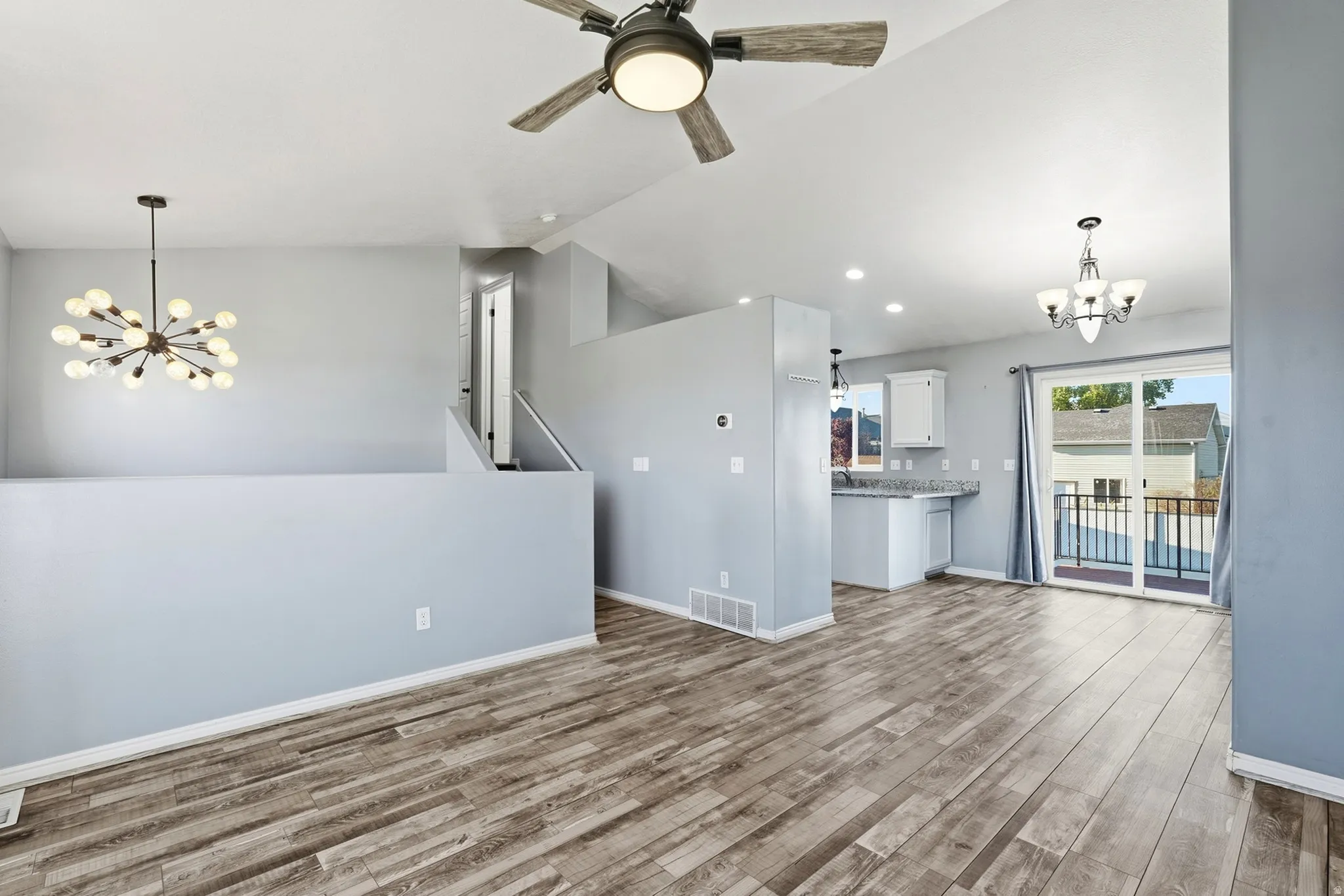 Vaulted ceilings with a ceiling fan, wood-finish flooring, modern chandelier, recessed lighting, and a sliding glass door to an exterior balcony