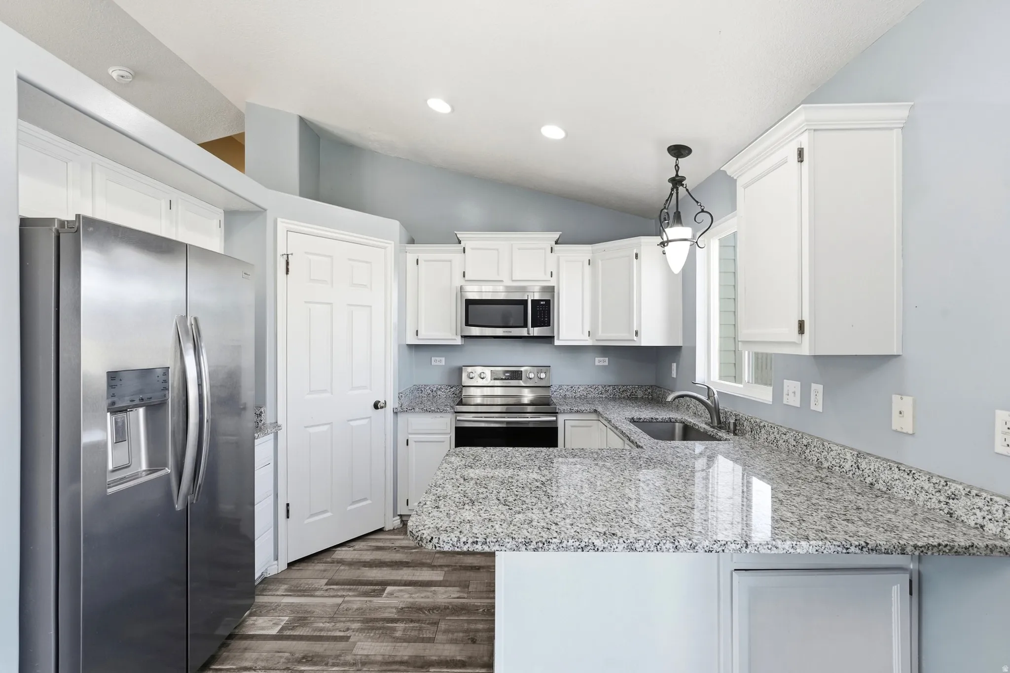 Kitchen featuring white cabinetry, stainless steel appliances, granite countertops, wood-finish flooring, and vaulted ceilings