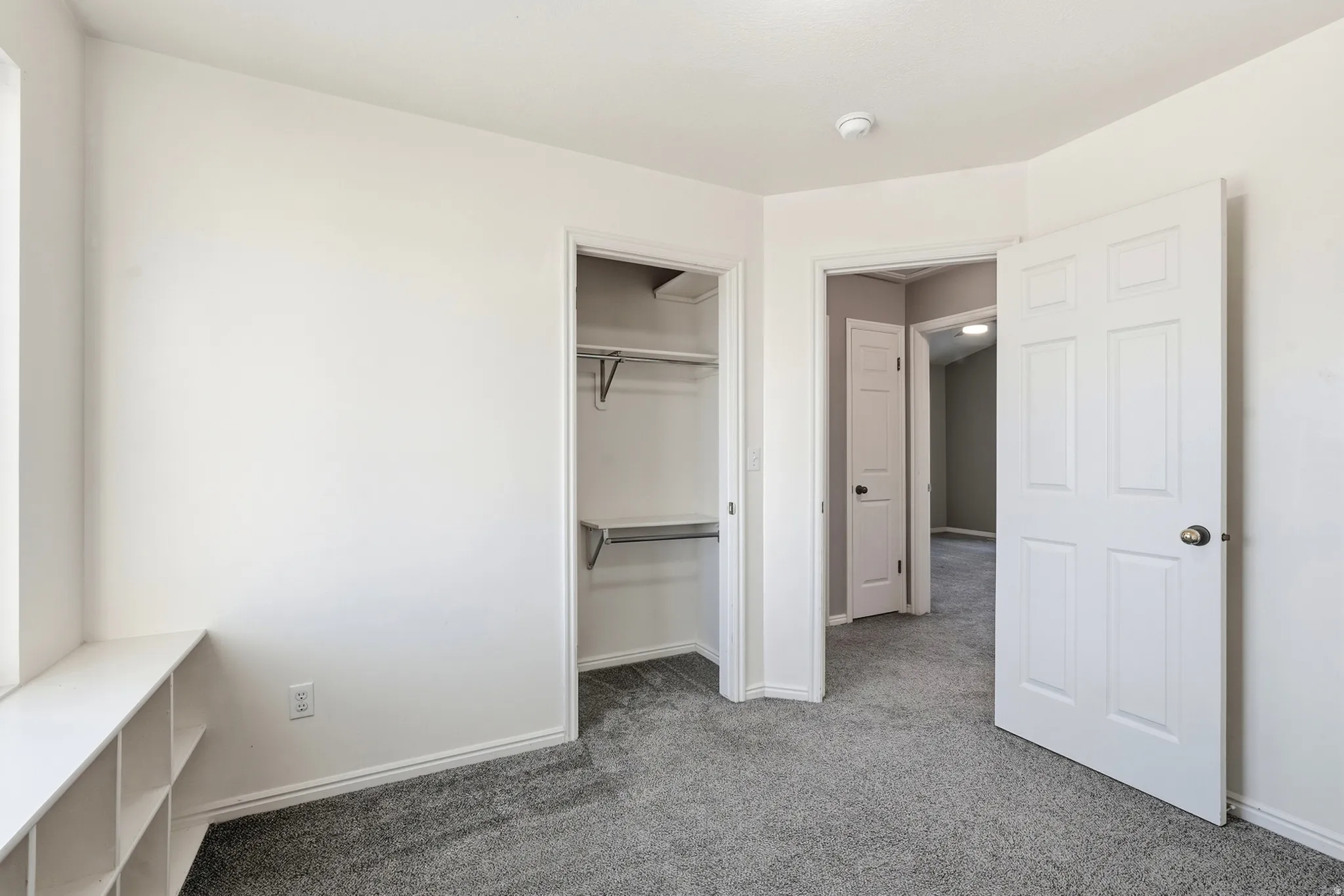 Built-in window bench with integrated shelving, plush grey carpeting, walk-in closet with shelving and hanging rods, white paneled doors, and neutral wall tones