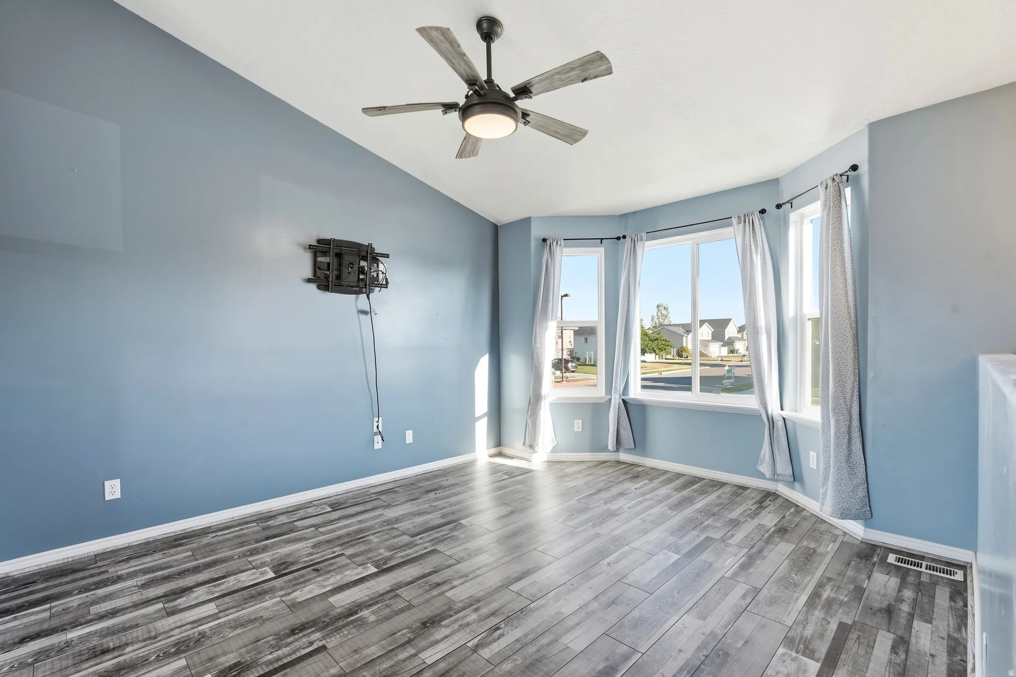 Bay window with multiple panes, wood-finish flooring, ceiling fan with integrated lighting, and light blue wall finish