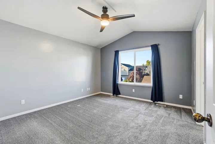 Vaulted ceiling with an attached ceiling fan, dual-pane window, and wall-to-wall carpeting