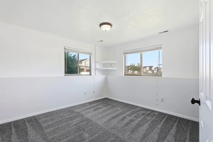 Recessed windows, wall-mounted shelving, overhead flush-mount lighting, and gray patterned carpeting