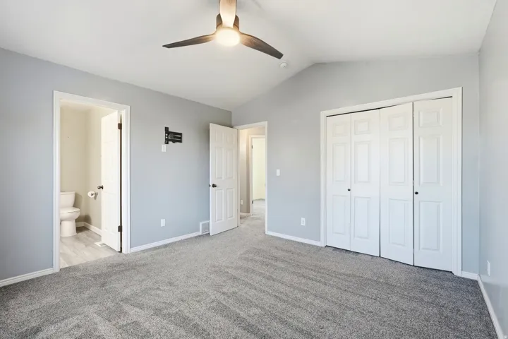 Vaulted ceiling with a ceiling fan, plush gray carpeting, light gray wall paint, white bi-fold closet doors, and a wall-mounted TV bracket