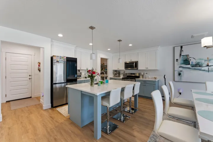Modern kitchen featuring white upper cabinetry, blue-grey base cabinetry, stainless steel appliances, a center island with seating, and wood-finish flooring
