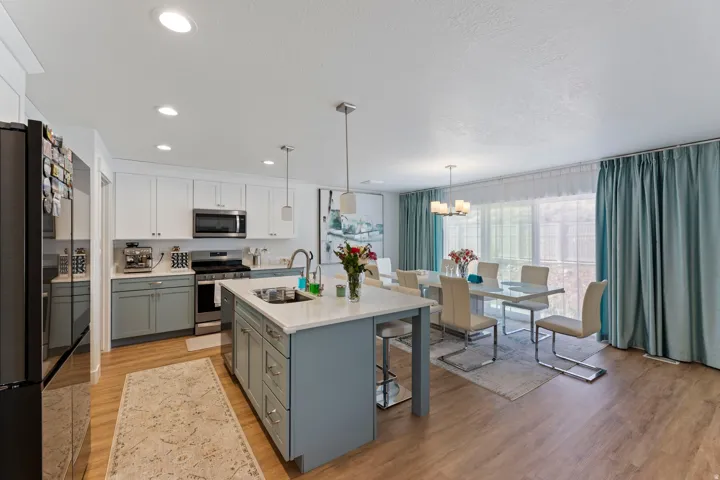 Kitchen featuring white upper cabinetry, gray lower cabinetry, stainless steel appliances, and an island with a sink