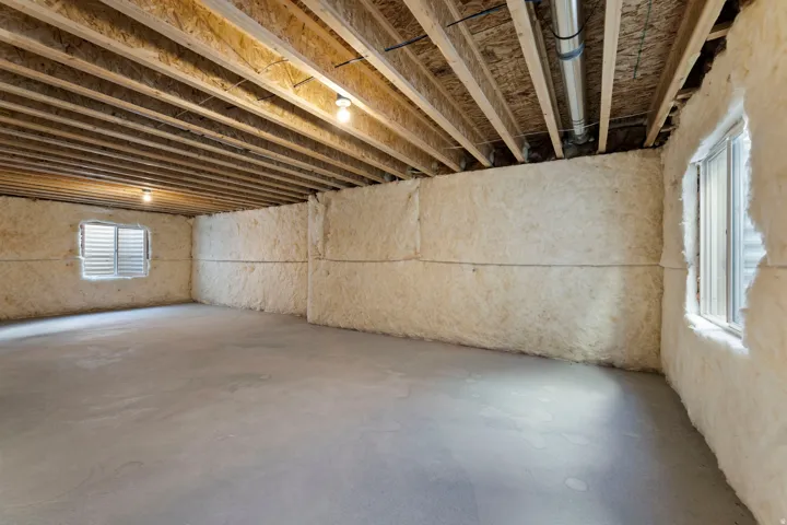 Spacious basement featuring exposed beam ceiling with recessed lighting, concrete flooring, and natural light from multiple windows