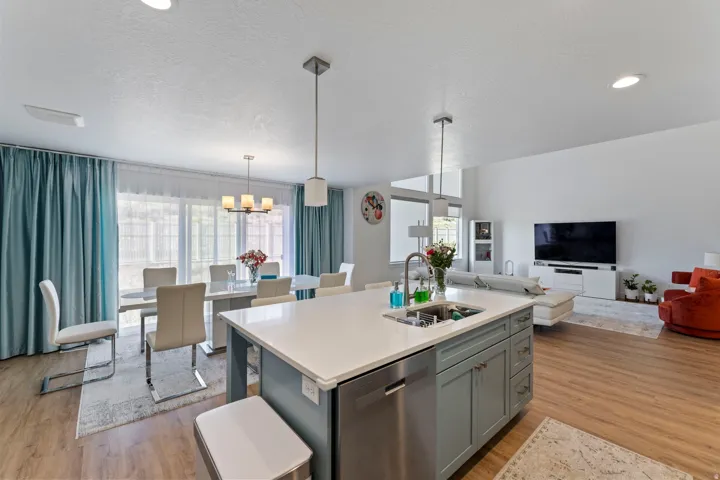 Open-concept living space with wood-finish flooring, a kitchen island with integrated sink, recessed lighting, and a dining area with direct outdoor access