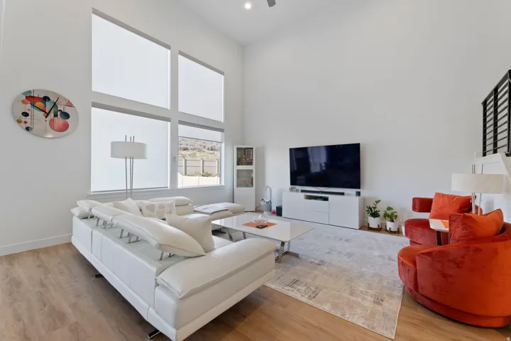 Vaulted ceiling, full-height window wall with roller shades, wood-finish flooring, built-in media console, and staircase with metal railings