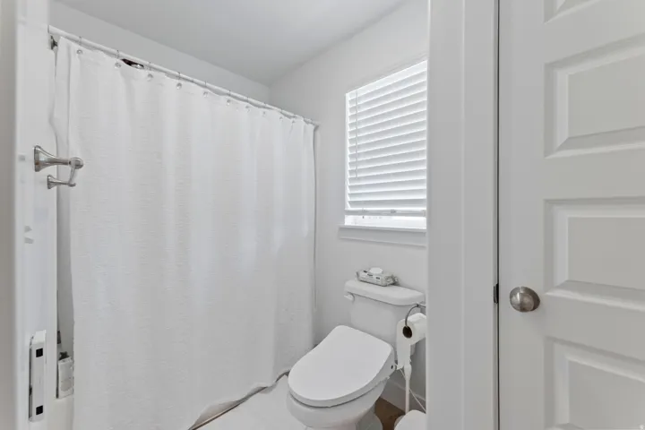 Bathroom featuring a window with privacy blinds, a built-in toilet, and a shower area