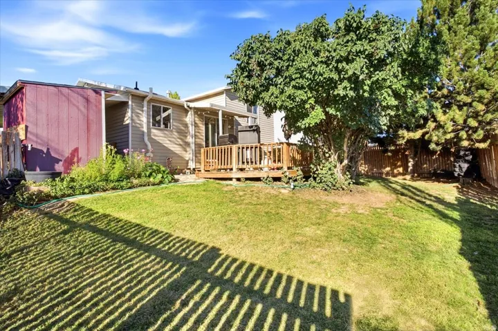 Expansive grass lawn with a wood deck, mature trees, and a privacy fence