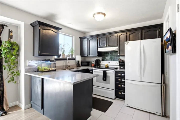 Kitchen with dark cabinetry, light-toned granite countertops, a full suite of white appliances, a tiled backsplash, and recessed lighting