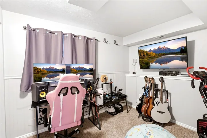 Recessed ceiling detail, wall-mounted television, wainscoting, and carpeted flooring