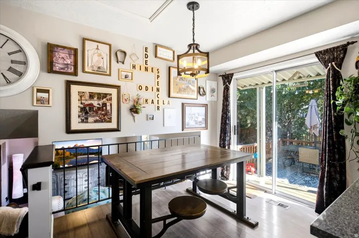 Wood-finish flooring throughout, sliding glass door with exterior access, contemporary hanging light fixture, black metal railing, and an exterior deck with a covered area