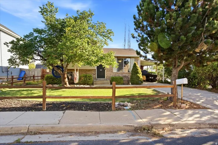 Brick exterior with a dark front door, mature trees, a manicured lawn, and a split-rail fence