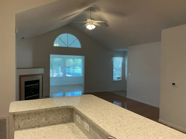 Vaulted ceilings with a ceiling fan, a fireplace with a tile surround and wood mantel, an arched transom window, and a stone-finish countertop