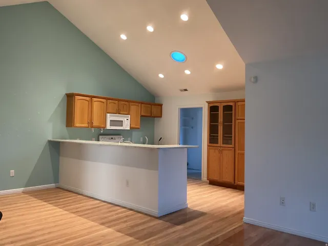 Vaulted ceiling with recessed lighting, wood-finish flooring, wood cabinetry, and a built-in microwave