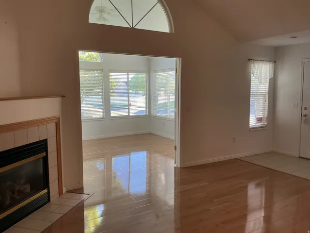 Vaulted ceiling with an arched transom window, wood-finish flooring, and a tiled fireplace