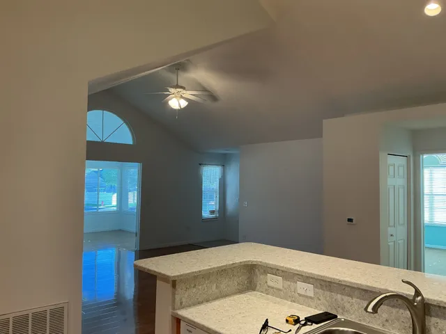 Vaulted ceiling with ceiling fan, arched transom window, wood-finish flooring, and a breakfast bar with stone-finish countertop