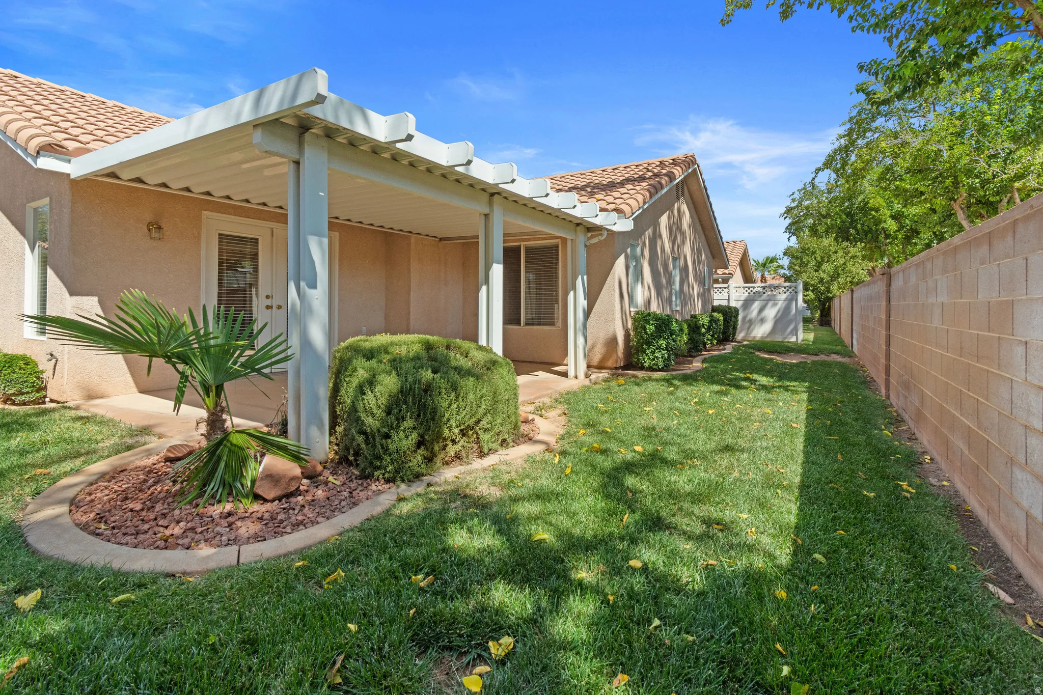 Expansive patio with an overhead pergola, green lawn, and privacy wall