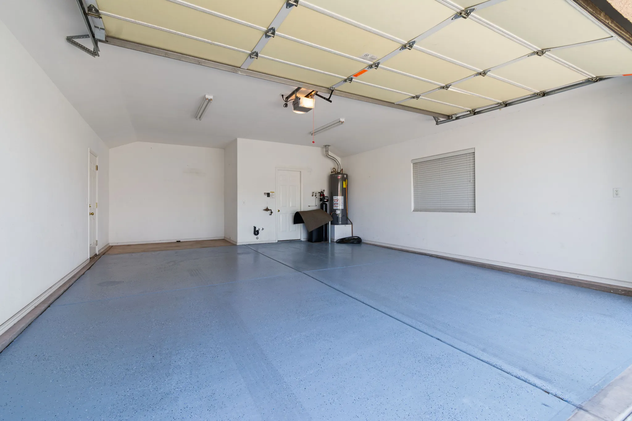 Spacious garage featuring an overhead door, painted concrete flooring, a water heater, a window with blinds, and fluorescent lighting