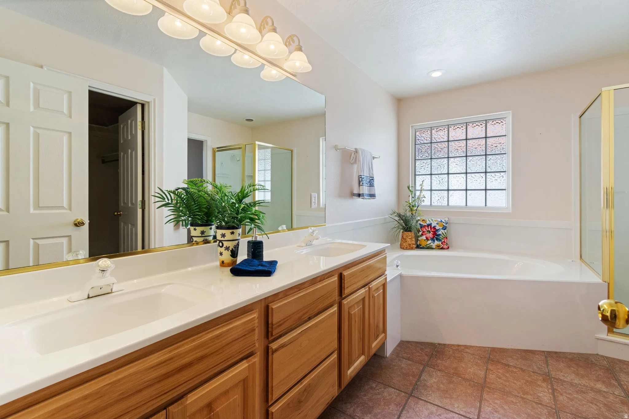 Dual vanity with integrated sinks, wood-finish cabinetry, built-in bathtub, glass block window, and tile flooring