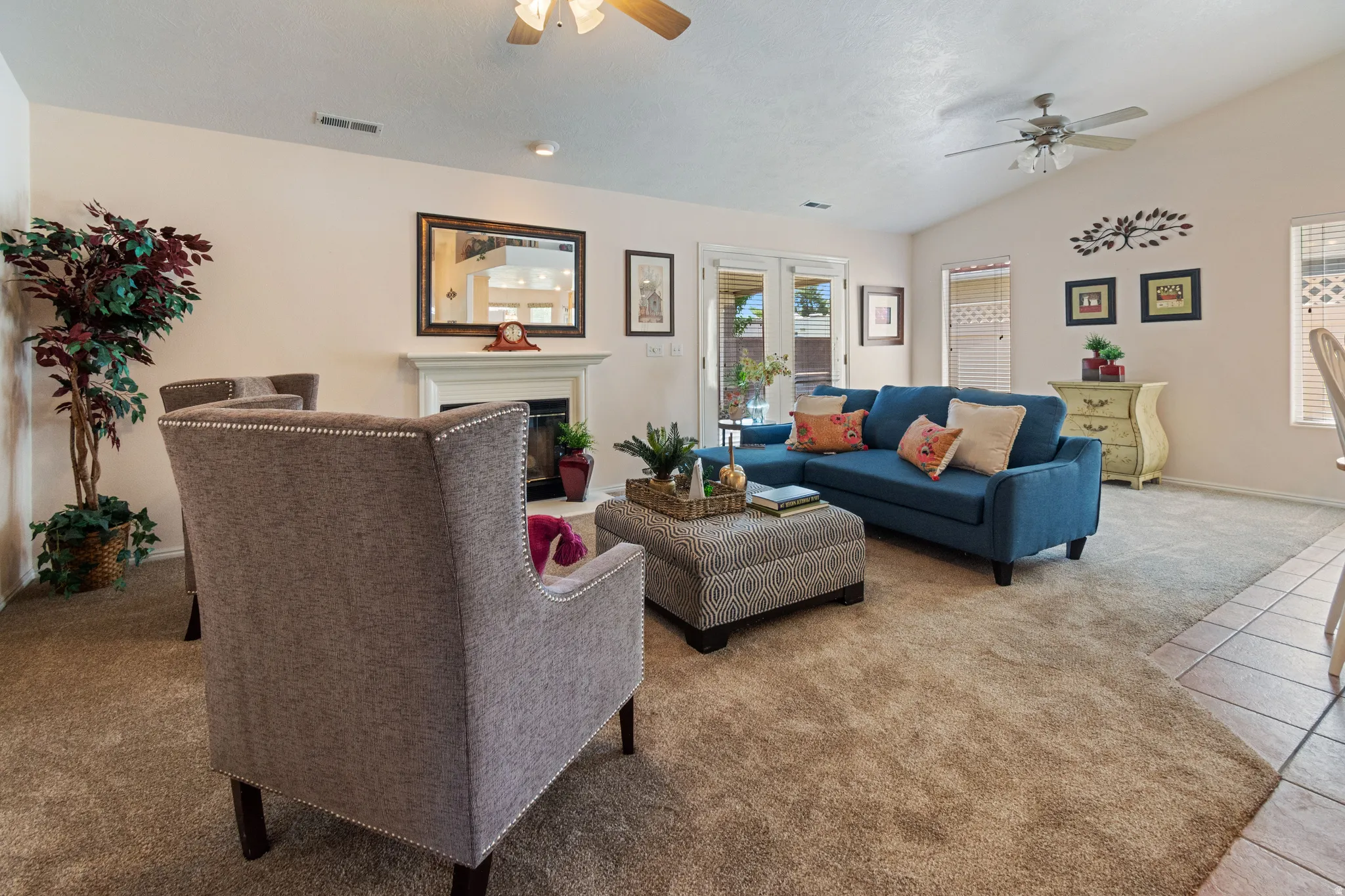 Vaulted ceiling, ceiling fans, white fireplace with mantle, French doors, and tile flooring