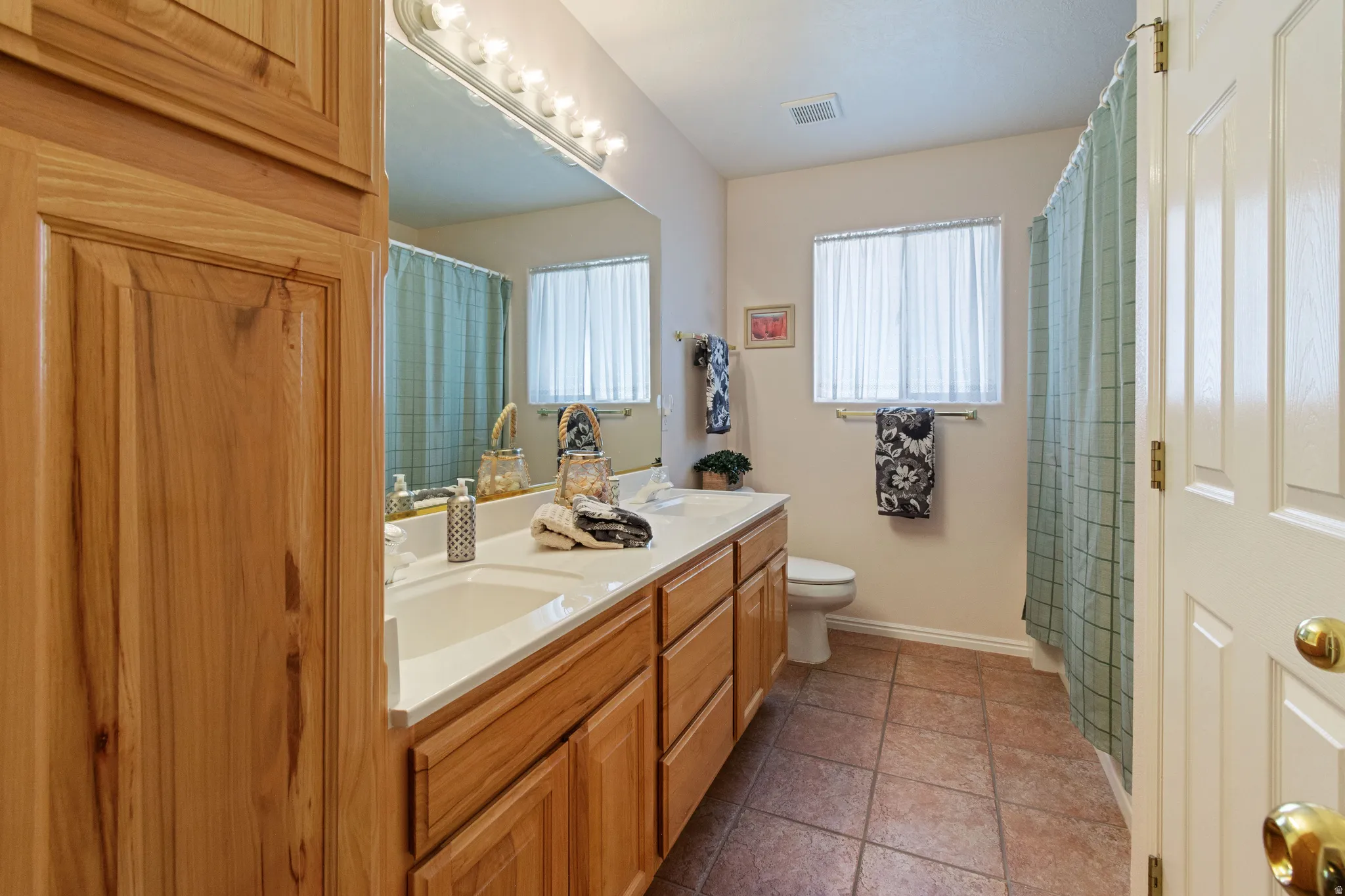 Dual vanity with integrated sinks, wood cabinetry, tile flooring, and a built-in storage cabinet