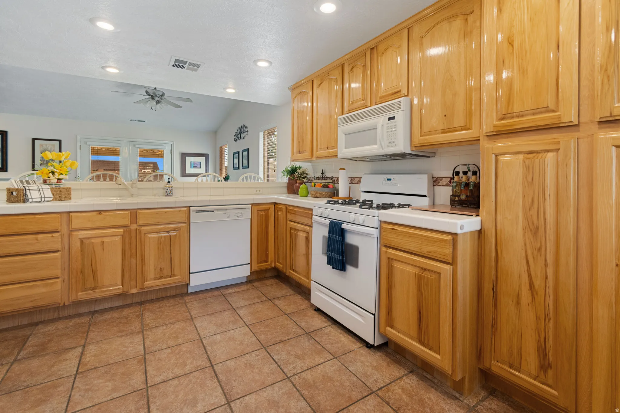 Kitchen featuring wood cabinetry, white appliances, white countertops, tile flooring, and a tile backsplash