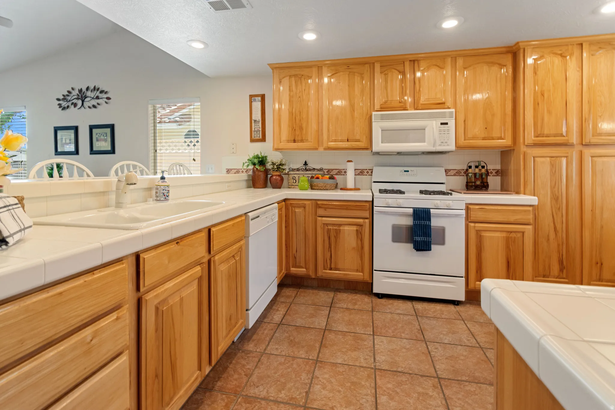 Kitchen featuring wood cabinetry, tile countertops, integrated double basin sink, white appliances, and tile flooring