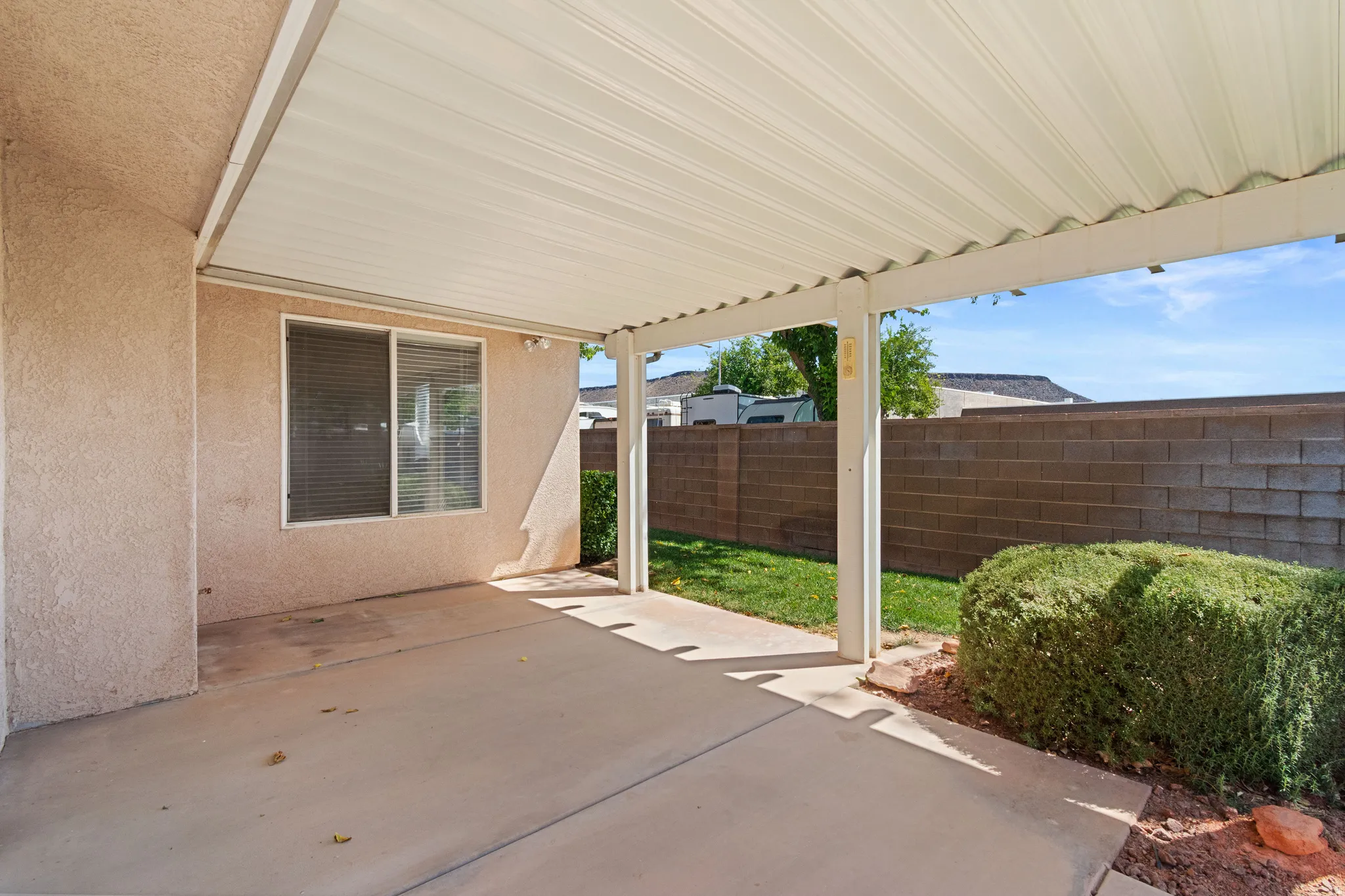 Concrete patio with an attached covered awning, stucco exterior, and a block wall perimeter