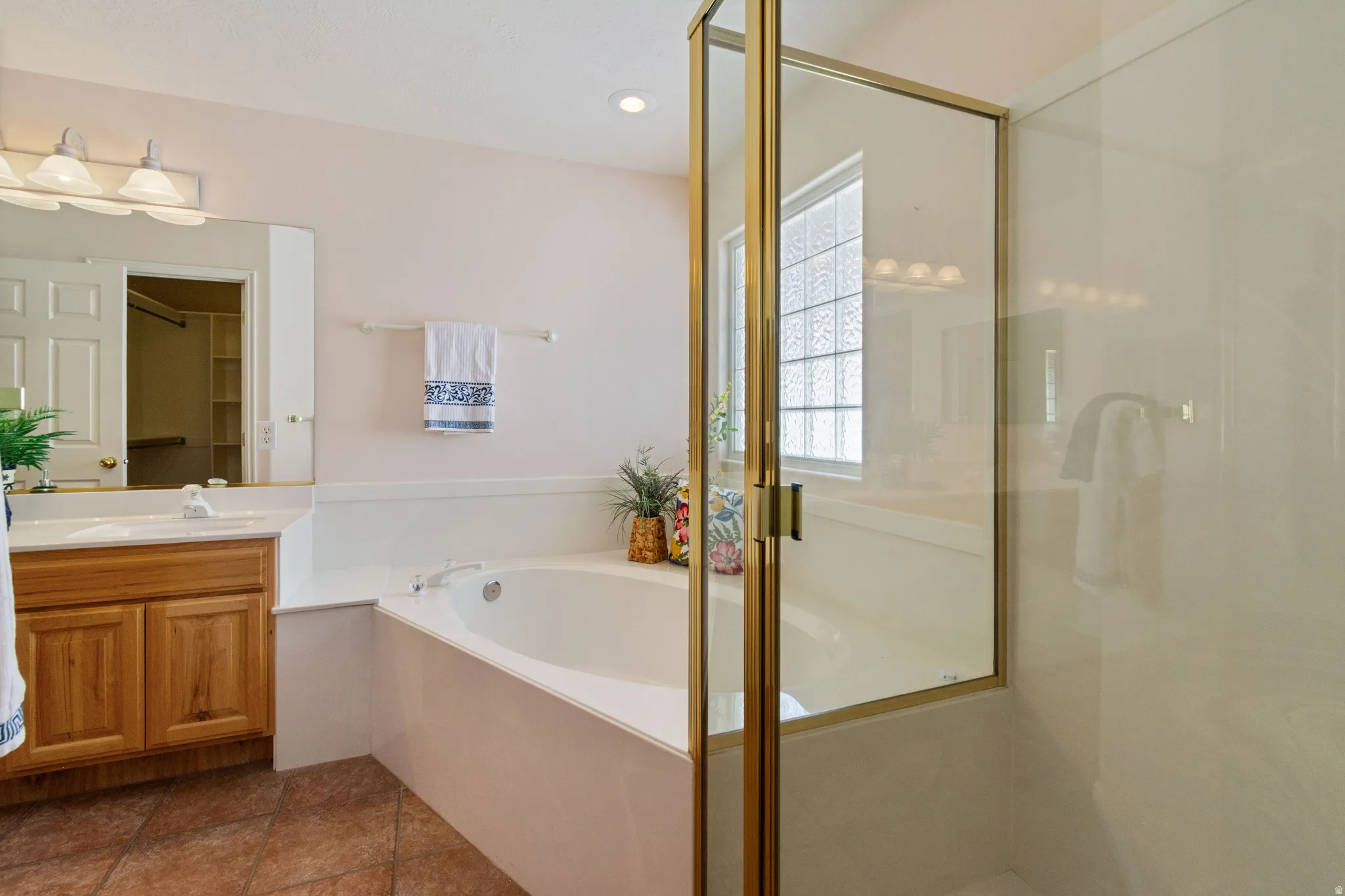 Spacious bathroom featuring a built-in soaking tub, a separate glass-enclosed shower, a vanity with wood-finish cabinetry, and a large mirror