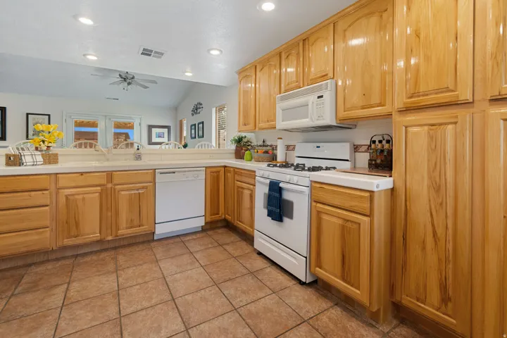 Kitchen featuring wood cabinetry, white appliances, white countertops, tile flooring, and a tile backsplash