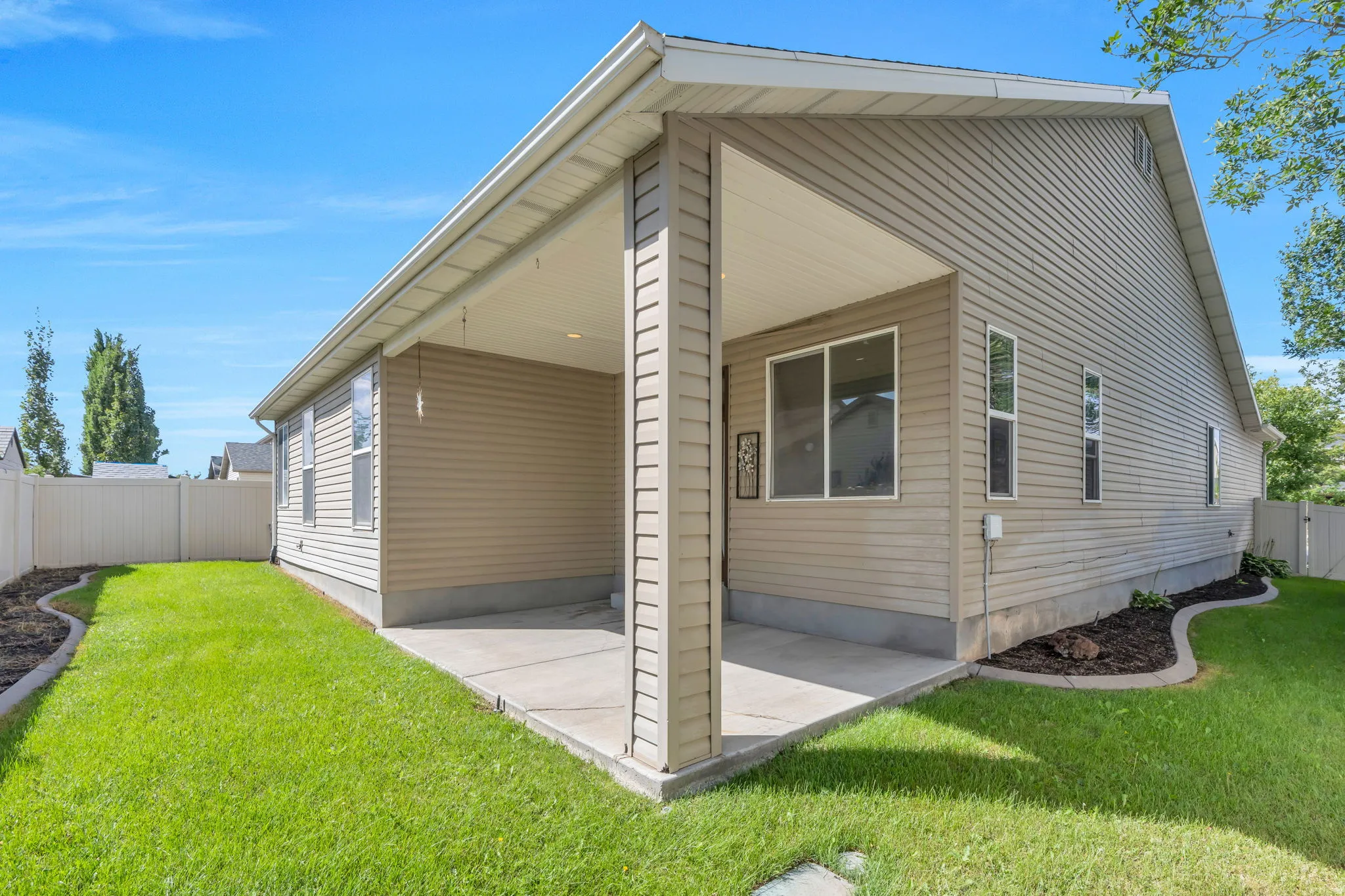 Covered concrete patio with recessed lighting, vinyl siding exterior, and landscaped garden beds