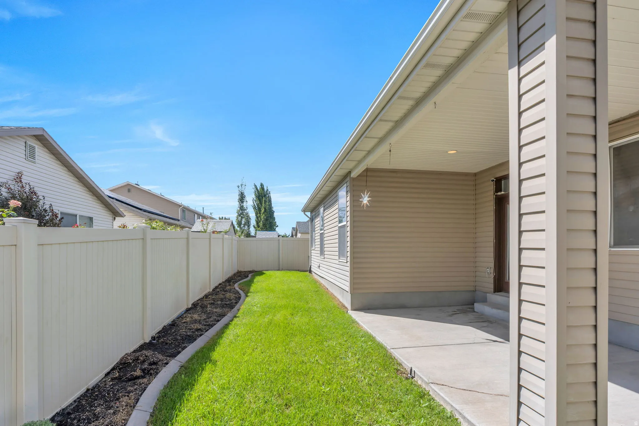 Manicured lawn with a defined landscape bed, full privacy fencing, and an exterior covered patio